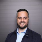 Portrait of Ahmed Khanji, Founder and CEO of Gridware, smiling in a navy jacket and light blue shirt.