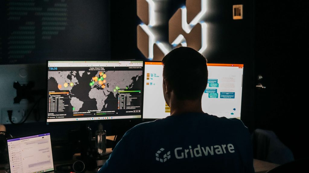 Gridware employee sitting in front of a computer screen with cyber threats pointed across a map of the world