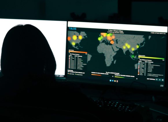 Gridware employee sitting at computer screen looking at world wide cyber threats pointed on a map